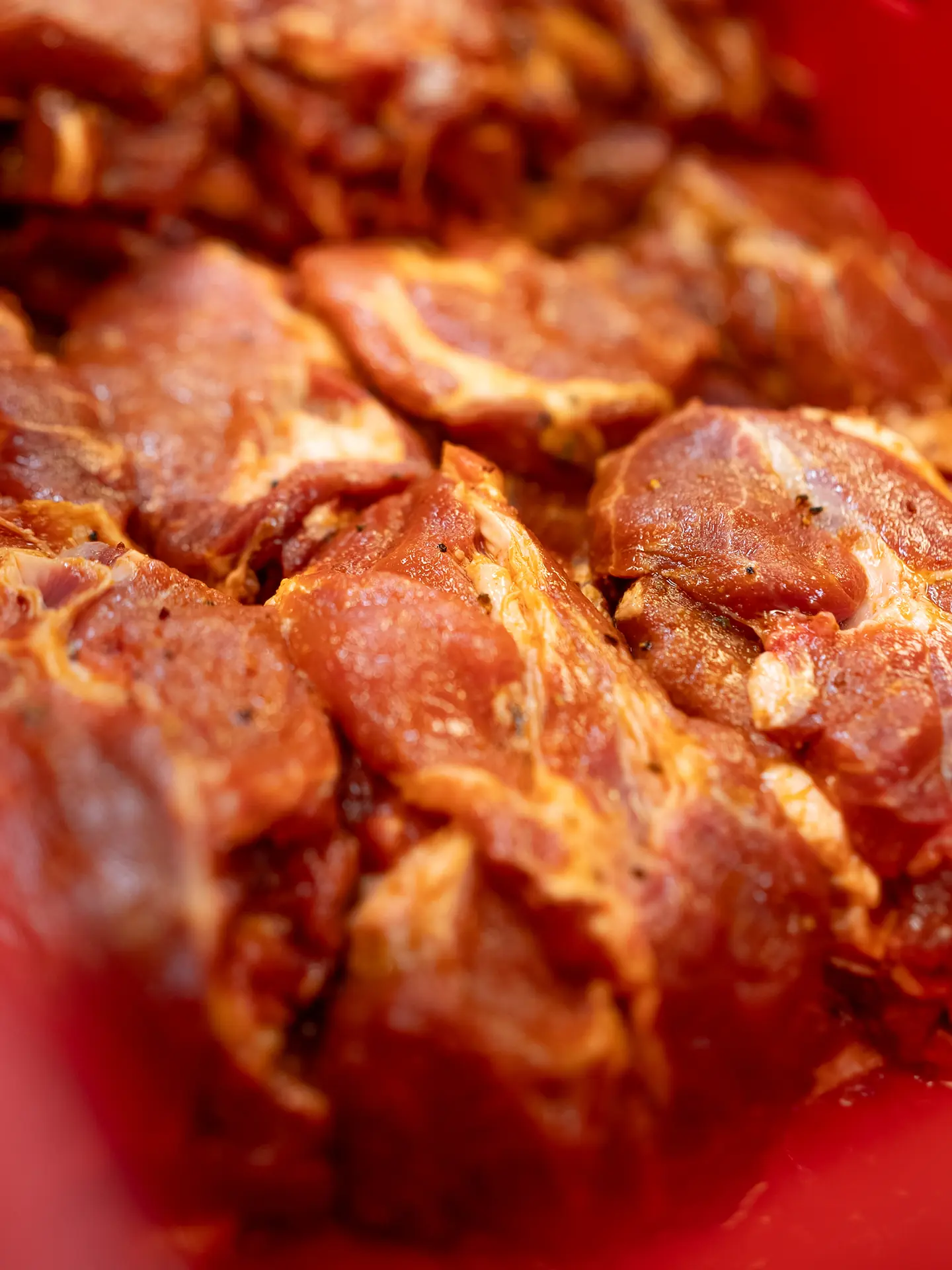 Eine Auswahl an Bio-Fleischstücken, darunter Braten, Keulen und Burger-Patties, auf einem Holzbrett, garniert mit Kräutern und Gewürzen.